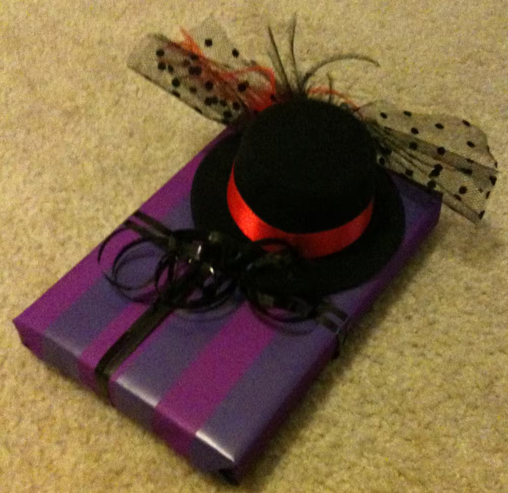 A wrapped gift with a hairclip with a tiny hat on it in the bow